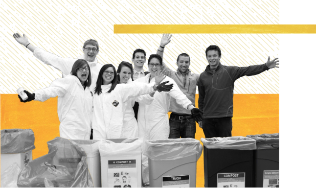  "A group of eight people pose together celebrating at what appears to be a waste sorting or recycling facility. Several people wear white protective coveralls or lab coats, while others are in casual clothing. They have their arms raised in celebration and are smiling at the camera. Behind them are various waste sorting bins and containers labeled for different types of materials including compost and trash. The image has a stylized design treatment with geometric shapes in orange and cream tones overlaying the black-and-white photograph.