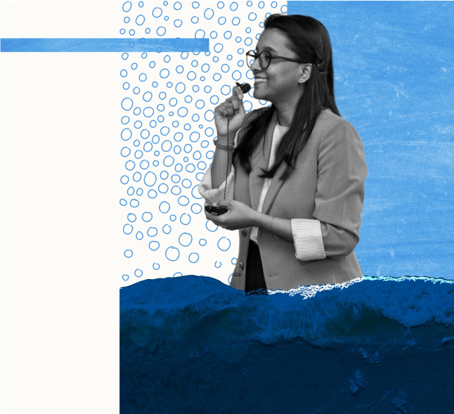 A woman with long dark hair and glasses smiles while speaking into a handheld microphone. She wears a light-colored blazer or cardigan and appears to be presenting or speaking at an event. The image features an artistic collage design with blue circular bubble patterns, geometric shapes, and what appears to be ocean waves or water imagery in blue tones at the bottom, creating a cohesive visual theme around water or marine topics